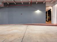 an open garage with exposed ceilings and floor lighting inside the building, and a grey wall behind