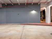 an open garage with exposed ceilings and floor lighting inside the building, and a grey wall behind