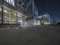 a parking lot with cars and trees on one side of the building at night with lighting on both sides