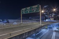 a freeway sign on the side of a road at night by a body of water