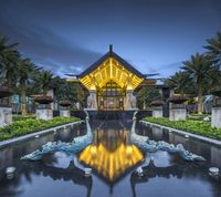 an illuminated gazebo with statues on it, sits between some water features and palm trees