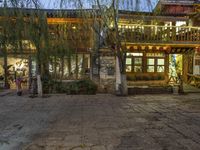 the view of people walking through the village at night time in the evening time, from the back of a house with wooden furniture