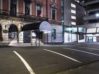 a bus stop on the street of a city at night with an umbrella attached to it