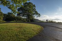 a park with benches, grass and trees next to the road in front of a hill