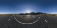 a panoramic view of an asphalt road with mountains in the background and the sun setting