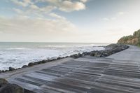 a wooden walkway runs down to the ocean as a boat sits in the water and rocks