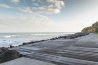 a wooden walkway runs down to the ocean as a boat sits in the water and rocks