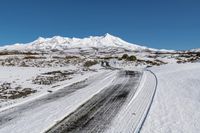 a road on snow - covered mountain side with snowy mountains in the background and tire tracks all around