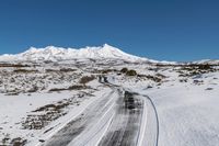 a road on snow - covered mountain side with snowy mountains in the background and tire tracks all around