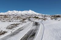 a road on snow - covered mountain side with snowy mountains in the background and tire tracks all around