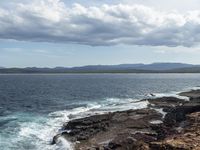 the ocean and the coastline near a cliff that has many rocks on it, and there is only one person in the water