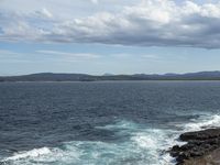 the ocean and the coastline near a cliff that has many rocks on it, and there is only one person in the water