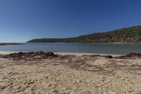 a couple of large rocks sitting on a sandy beach near water and some hills in the distance