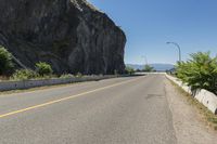 the sign points at a bend on the side of a road near the ocean and mountains