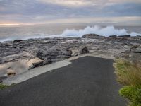 a paved pathway windscreens the crashing ocean at the edge of a beach side