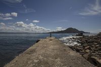 a lone pier at the ocean in front of mountains and water and clouds above it