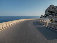 a long curved road going into the ocean with a motorcycle on it in front of it