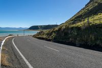 an empty road next to the ocean on a sunny day with mountains in the distance