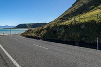 an empty road next to the ocean on a sunny day with mountains in the distance