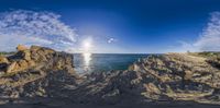 a panoramic view of the ocean with rocks and sand surrounding it and a cloudy sky