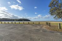 view of an empty parking lot overlooking water in the distance with clouds and grass at right