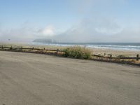 a person riding a bike on the beach side with fog rising from behind them and hills in the distance