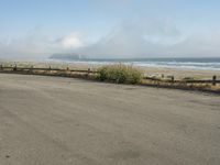 a person riding a bike on the beach side with fog rising from behind them and hills in the distance