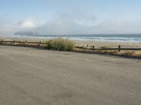 a person riding a bike on the beach side with fog rising from behind them and hills in the distance