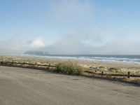 a person riding a bike on the beach side with fog rising from behind them and hills in the distance