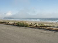 a person riding a bike on the beach side with fog rising from behind them and hills in the distance