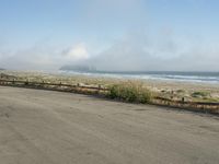 a person riding a bike on the beach side with fog rising from behind them and hills in the distance