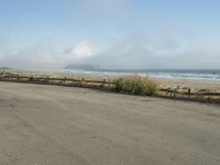 a person riding a bike on the beach side with fog rising from behind them and hills in the distance