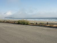 a person riding a bike on the beach side with fog rising from behind them and hills in the distance