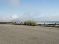 a person riding a bike on the beach side with fog rising from behind them and hills in the distance