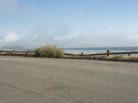 a person riding a bike on the beach side with fog rising from behind them and hills in the distance