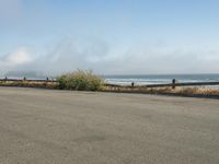 a person riding a bike on the beach side with fog rising from behind them and hills in the distance