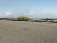 a person riding a bike on the beach side with fog rising from behind them and hills in the distance