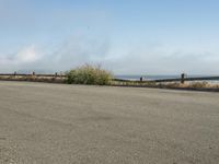 a person riding a bike on the beach side with fog rising from behind them and hills in the distance