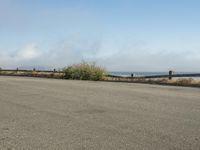 a person riding a bike on the beach side with fog rising from behind them and hills in the distance