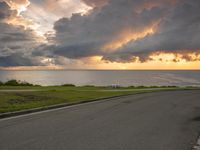 a view of the ocean from a cliff road at sunset with dramatic clouds and sun rays