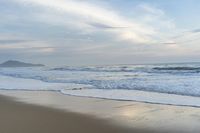 an ocean view of a sandy beach, waves lapping on the shore and distant clouds in the sky