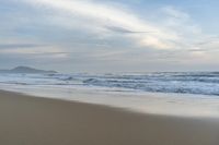 an ocean view of a sandy beach, waves lapping on the shore and distant clouds in the sky