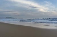 an ocean view of a sandy beach, waves lapping on the shore and distant clouds in the sky