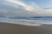 an ocean view of a sandy beach, waves lapping on the shore and distant clouds in the sky