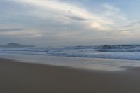 an ocean view of a sandy beach, waves lapping on the shore and distant clouds in the sky