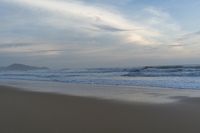 an ocean view of a sandy beach, waves lapping on the shore and distant clouds in the sky