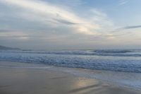 an ocean view of a sandy beach, waves lapping on the shore and distant clouds in the sky