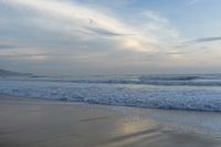 an ocean view of a sandy beach, waves lapping on the shore and distant clouds in the sky