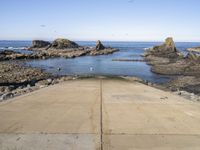 a paved sidewalk leading into the ocean and some rocky cliffs in the background of the ocean