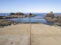 a paved sidewalk leading into the ocean and some rocky cliffs in the background of the ocean